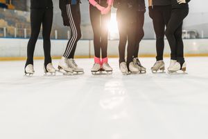 Group of skaters in protective gear practicing on an indoor ice rink.